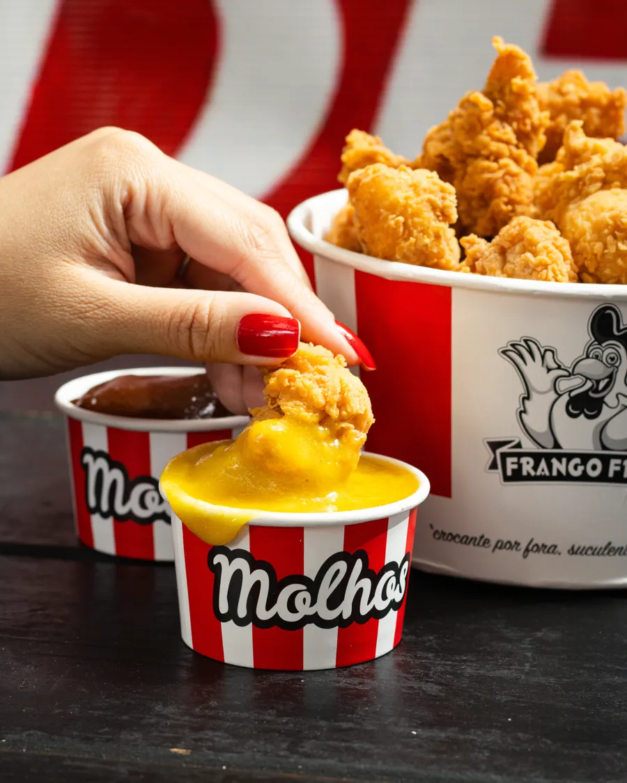 Mão molhando frango frito no pote de molho
