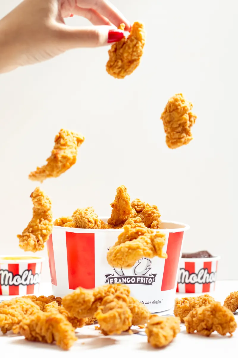 Pedaços de frango frito caindo no balde