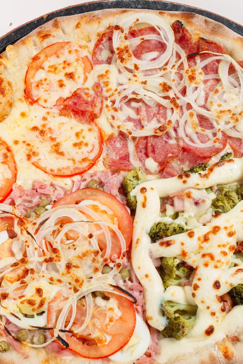 Close de pizza meio a meio com tomate e brócolis